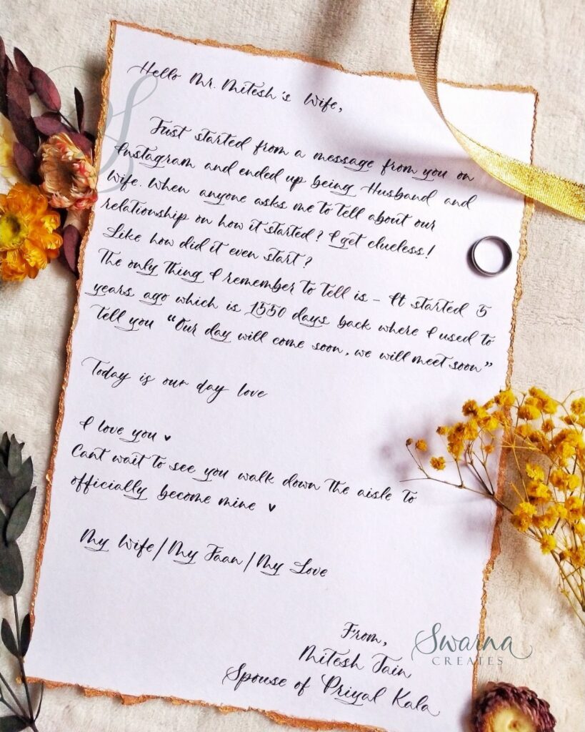 Handwritten love letter with gold edges surrounded by dried flowers and a ring.