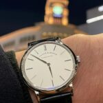 Silver wrist watch with white face and black leather strap on a wrist