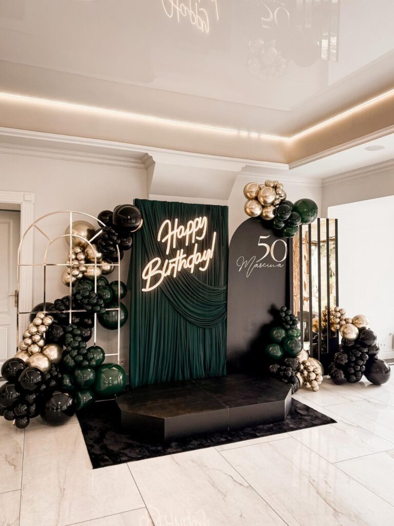 Elegant 50th birthday party decoration with green and gold balloons and backdrops.
