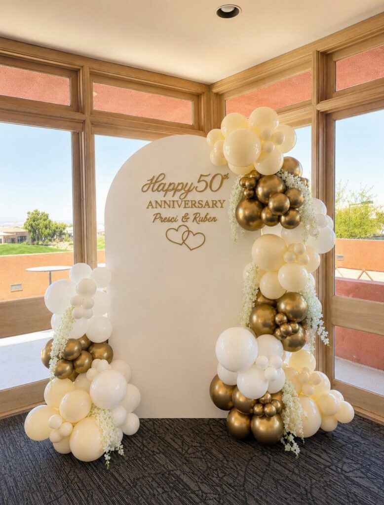 White arched backdrop with gold 50th anniversary text and gold and white balloons.