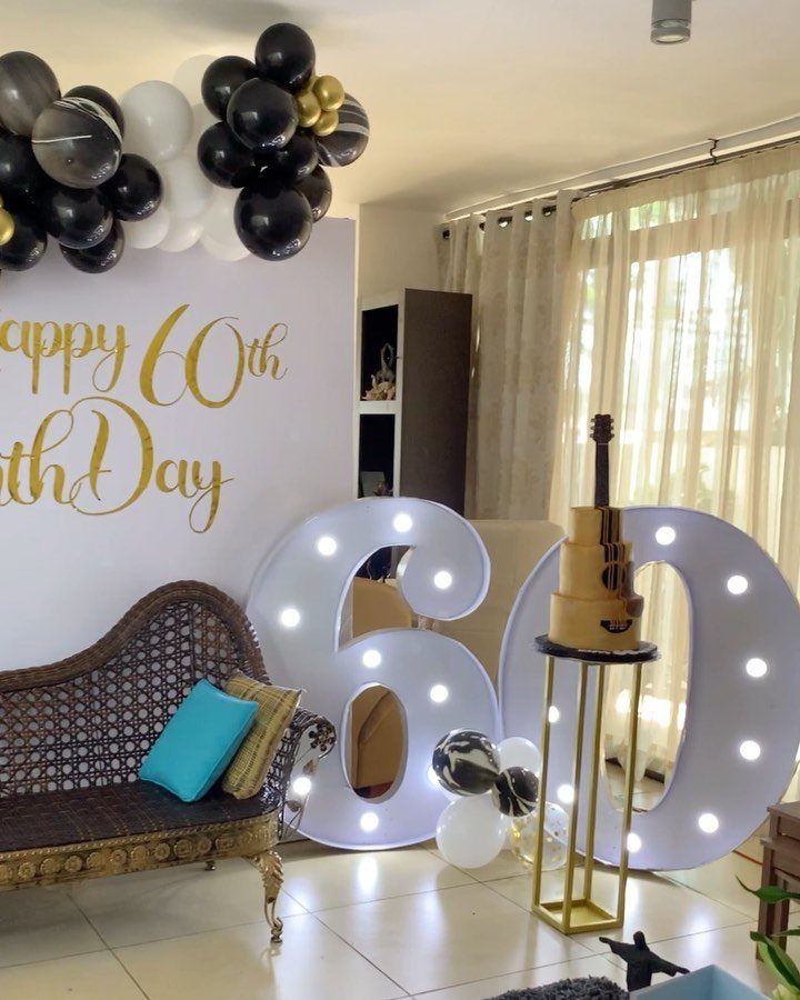 Birthday party decoration with large glowing 60 numbers, gold cake, and balloons.