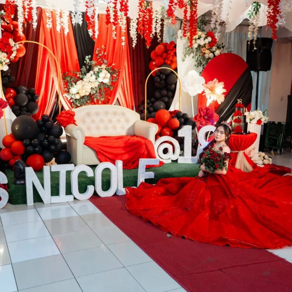 Young woman in red gown posing at an 18th birthday party with red decorations.