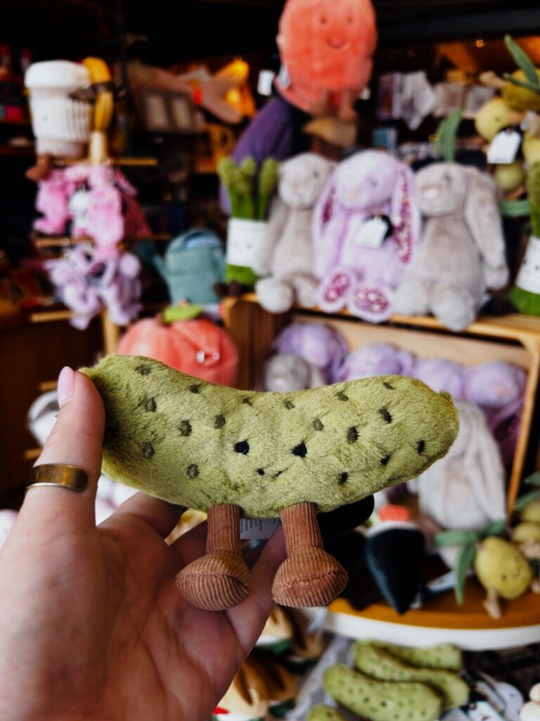 Green plush pickle toy with brown legs held in a person's hand.