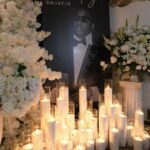 Memorial display with a large portrait, white pillar candles, and white floral arrangements.