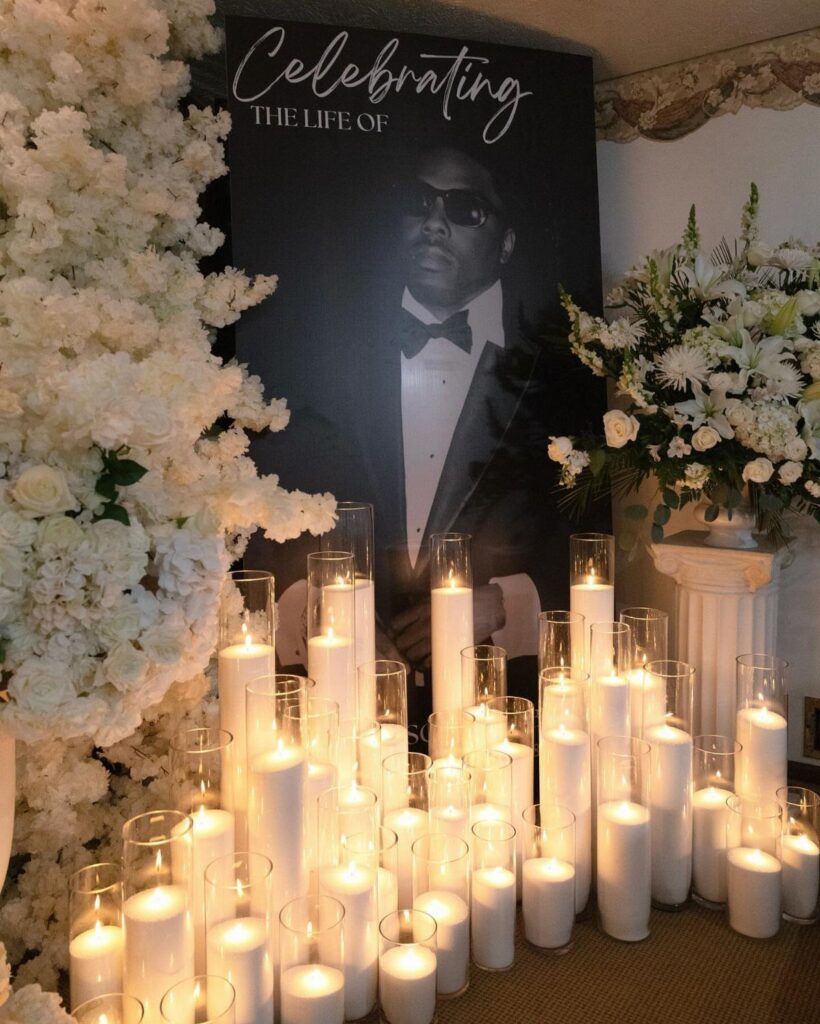 Memorial display with a large portrait, white pillar candles, and white floral arrangements.