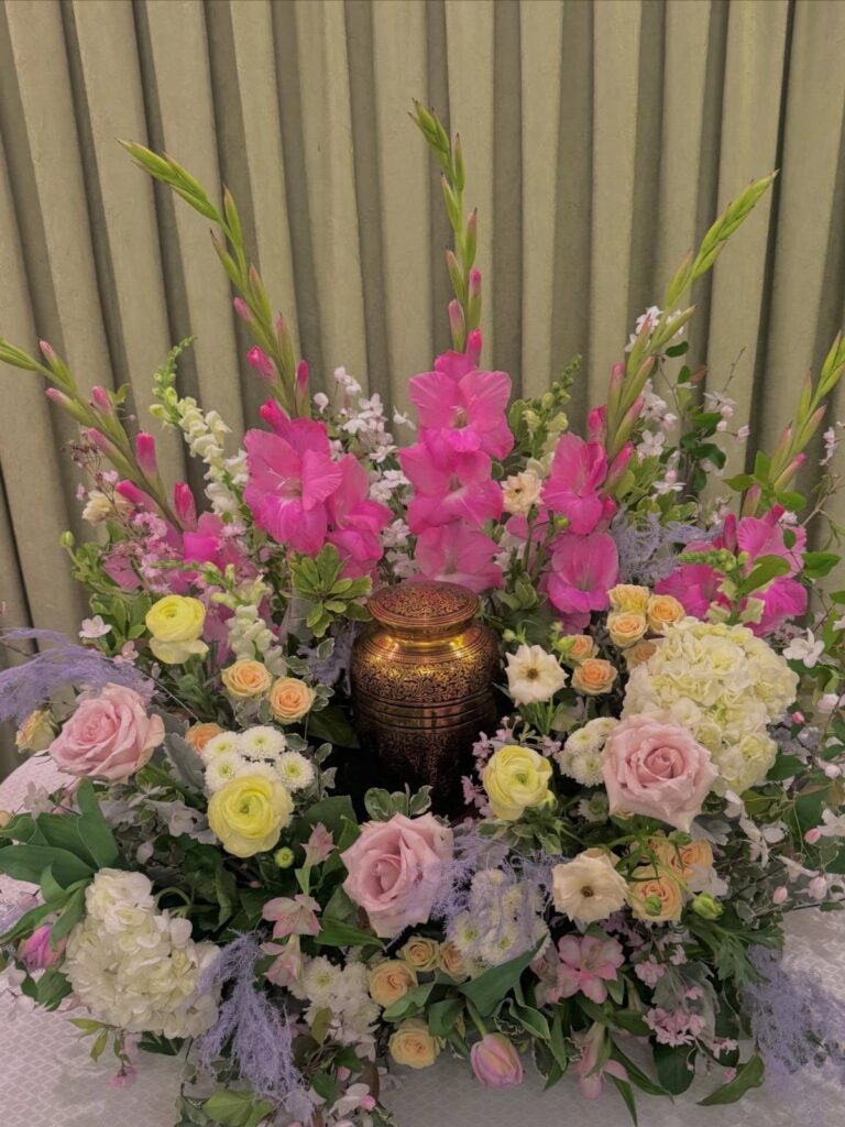 Floral arrangement with pink and yellow flowers surrounding a gold cremation urn.
