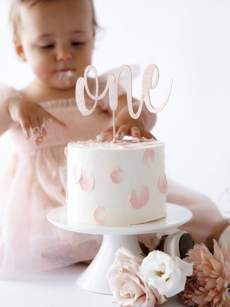 Baby girl in pink dress with a white smash cake and one topper