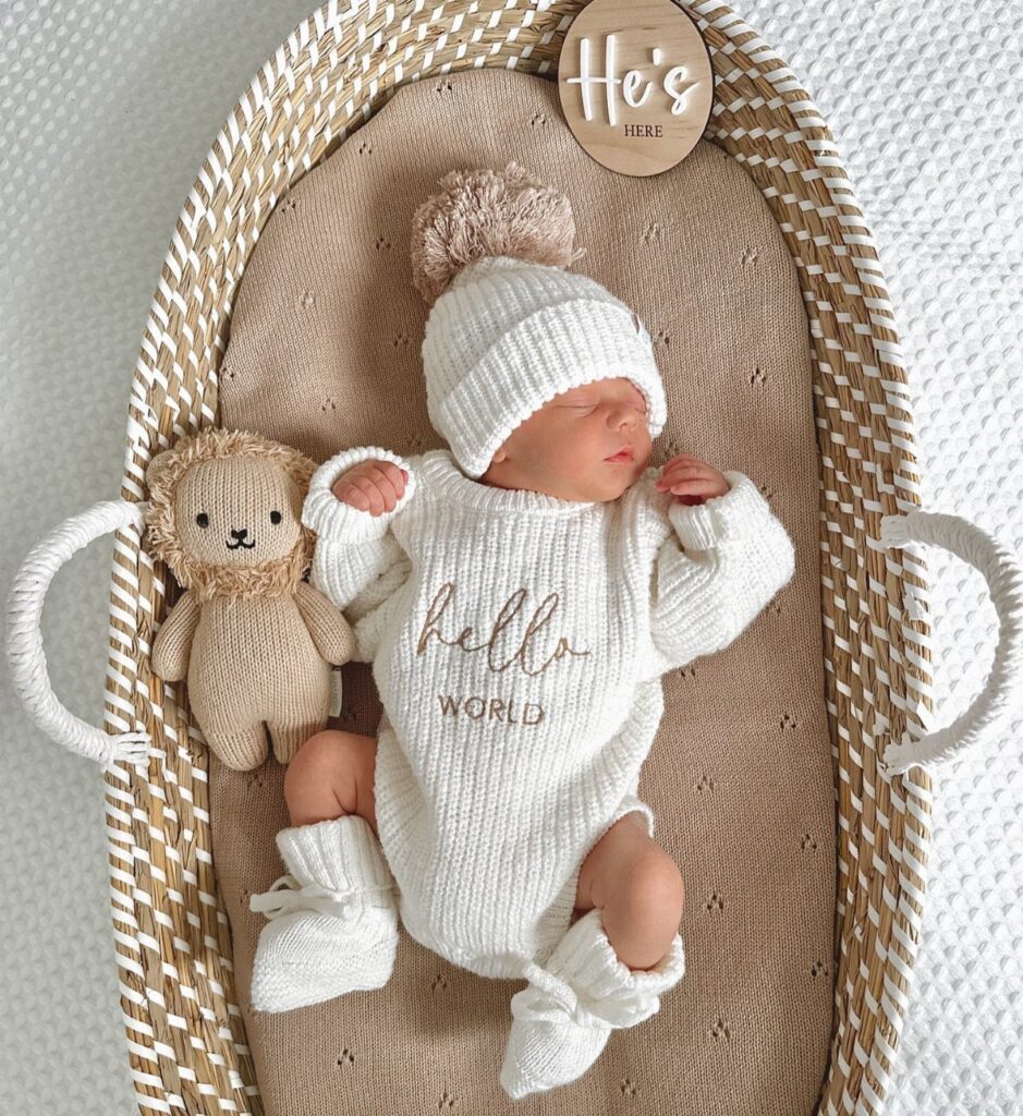 Newborn baby in white ribbed knit outfit and beanie lying in woven bassinet