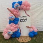 Baseball-themed gender reveal backdrop with pink and blue balloons and Dodgers baseballs.