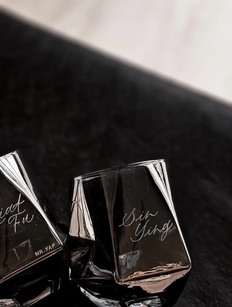 Two black engraved square glasses with cursive names on a dark surface.