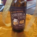 Beer bottle with custom 40th birthday label wrapped in a gold glittery ribbon.