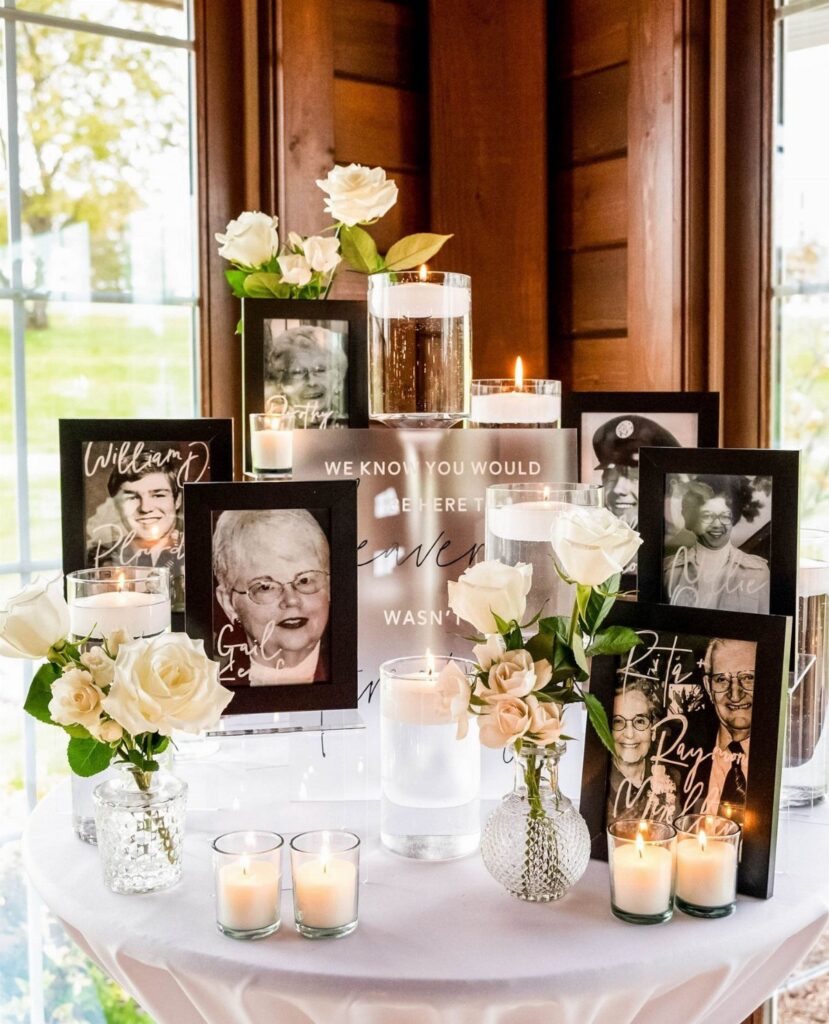 Memory table with framed portraits, white roses, and lit candles on white tablecloth.