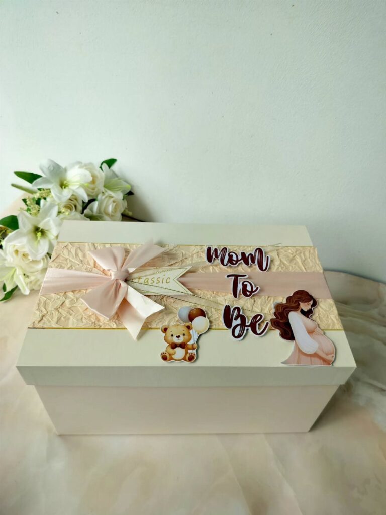 White gift box for a mom to be with pink bow and decorations.
