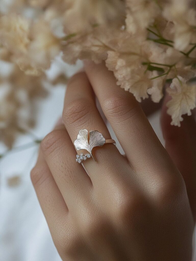 Silver ginkgo leaf ring on a finger with blurred white flowers in background