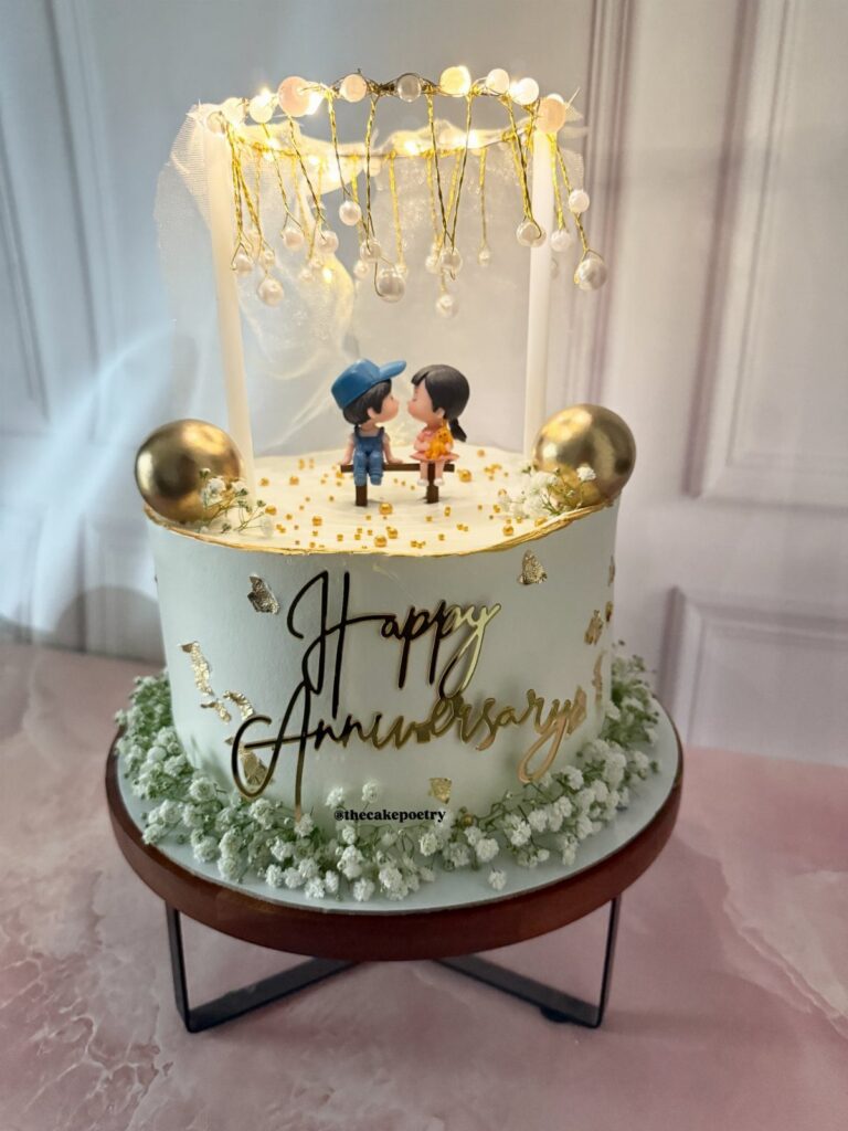 White anniversary cake with gold lettering, couple figurines, and baby's breath flowers.